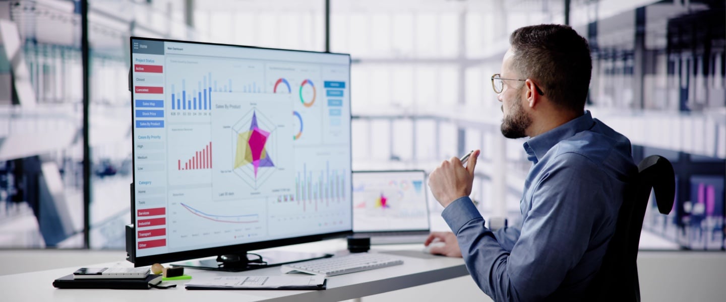 Man wearing glasses analyzing data dashboards and charts on a large monitor