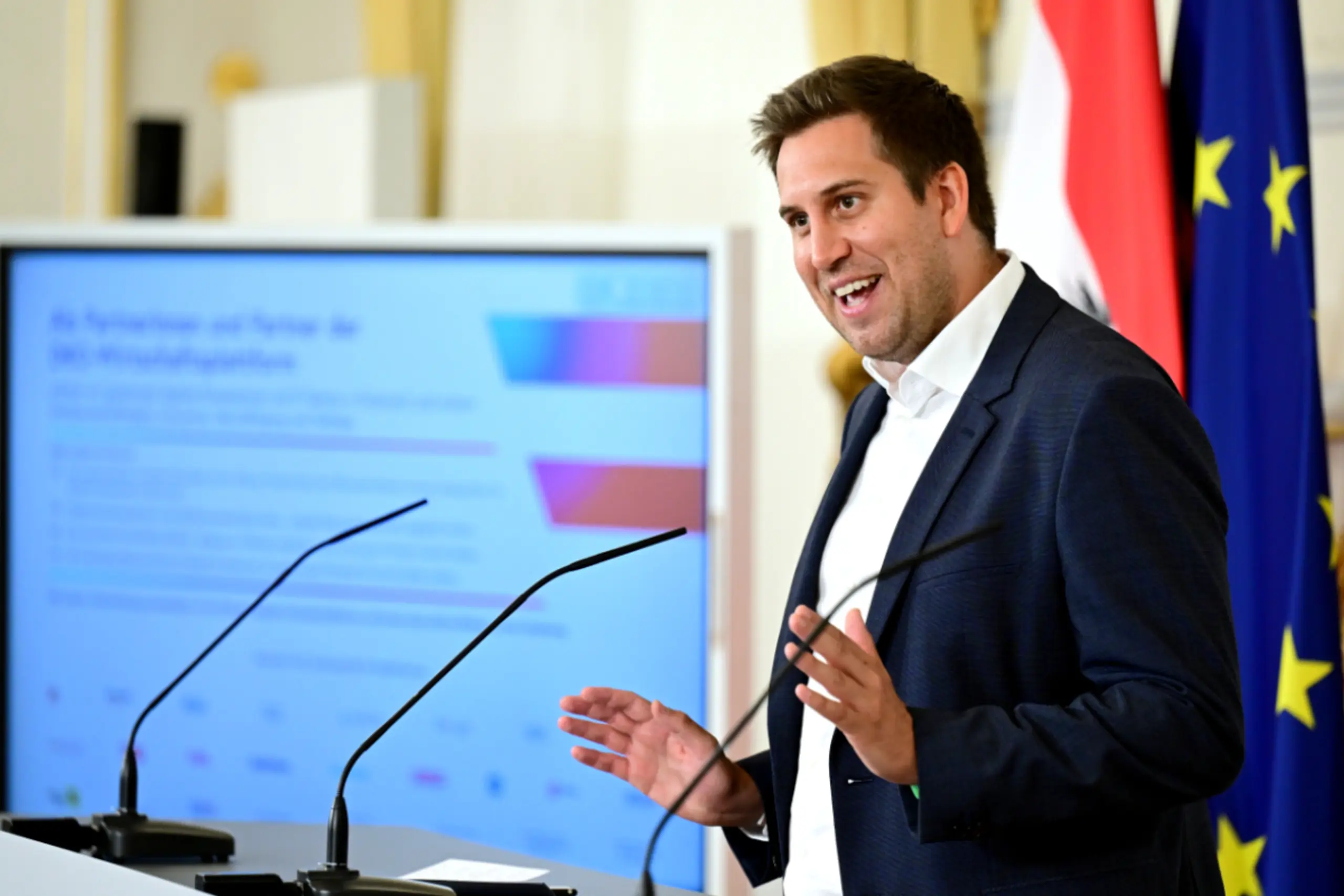 Austrian State Secretary Alexander Pröll announcing GovGPT at a press conference, with screens showing the AI interface